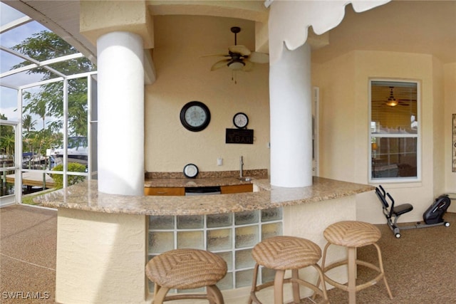 view of patio with glass enclosure, ceiling fan, and a bar