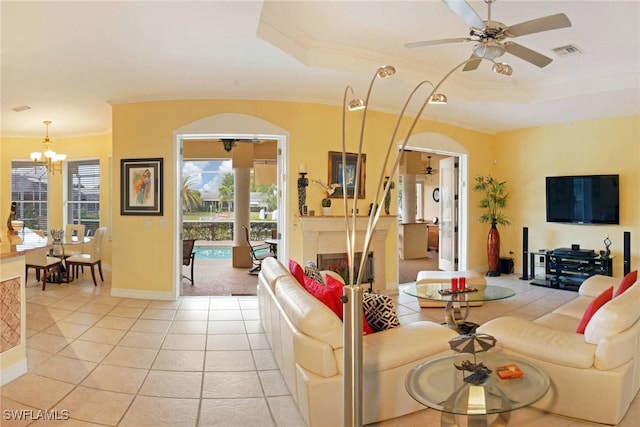 tiled living room with a raised ceiling, ceiling fan with notable chandelier, and ornamental molding