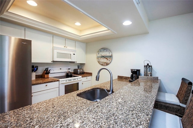 kitchen with white appliances, a tray ceiling, white cabinetry, and sink