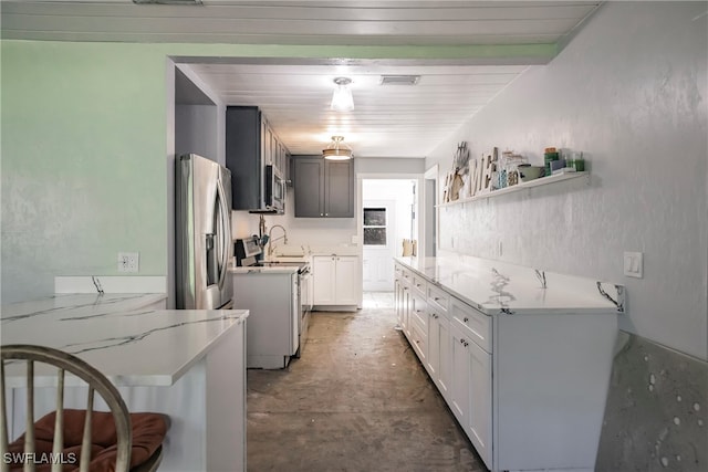 kitchen with white cabinets, concrete floors, light stone counters, kitchen peninsula, and stainless steel appliances