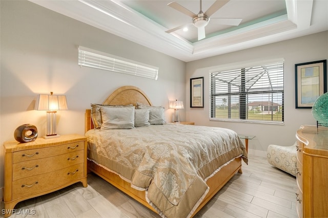 bedroom with ceiling fan, light hardwood / wood-style flooring, and a tray ceiling