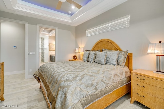 bedroom featuring a raised ceiling, light wood-type flooring, ensuite bath, and ceiling fan