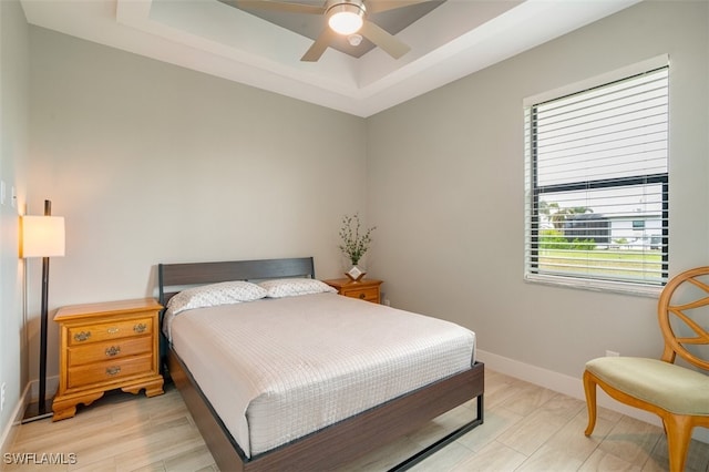 bedroom with ceiling fan, light wood-type flooring, and a tray ceiling