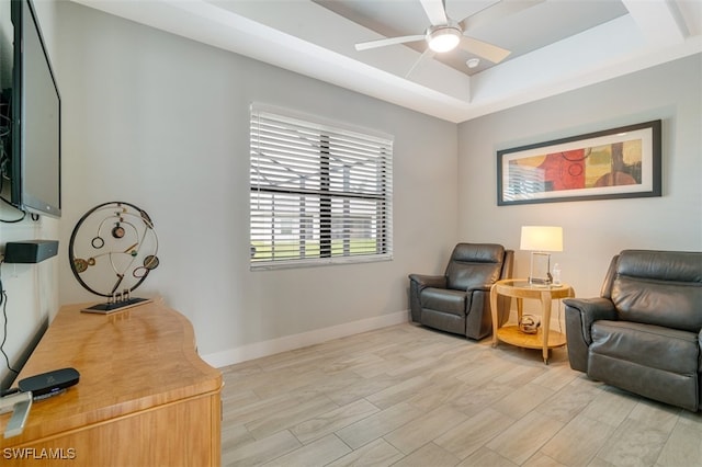 living area with a tray ceiling, light hardwood / wood-style flooring, and ceiling fan