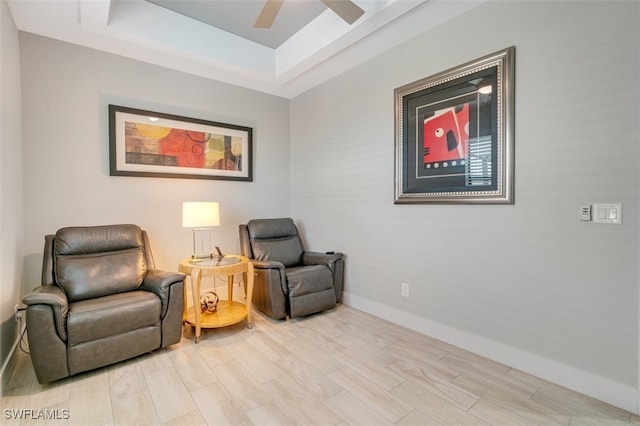 sitting room with ceiling fan, a raised ceiling, and light wood-type flooring