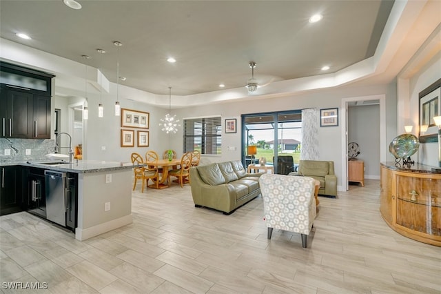 living room featuring ceiling fan with notable chandelier, a raised ceiling, light wood-type flooring, and sink