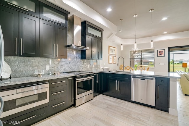 kitchen featuring light stone countertops, sink, wall chimney range hood, and appliances with stainless steel finishes