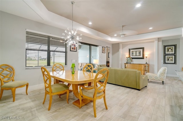 dining area with ceiling fan with notable chandelier, a raised ceiling, and light hardwood / wood-style flooring