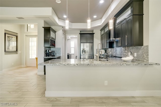 kitchen featuring kitchen peninsula, stainless steel fridge, light stone counters, and pendant lighting