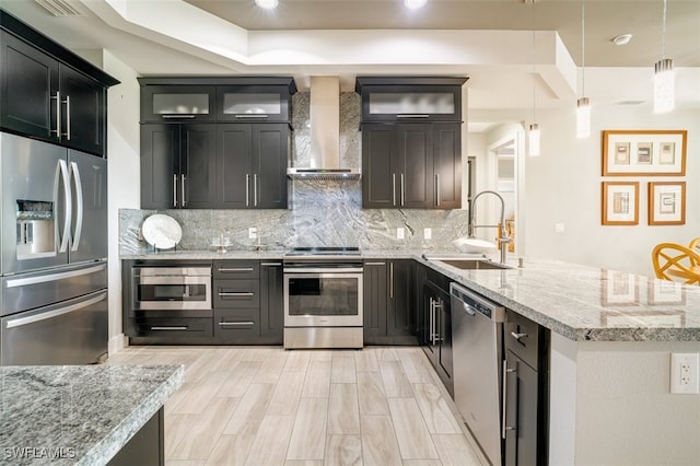 kitchen featuring sink, hanging light fixtures, wall chimney range hood, tasteful backsplash, and appliances with stainless steel finishes