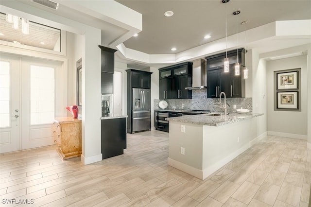 kitchen with kitchen peninsula, wall chimney range hood, sink, decorative light fixtures, and stainless steel fridge with ice dispenser