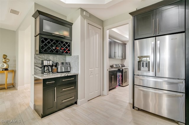 kitchen with light stone countertops, tasteful backsplash, washing machine and dryer, stainless steel fridge, and light wood-type flooring