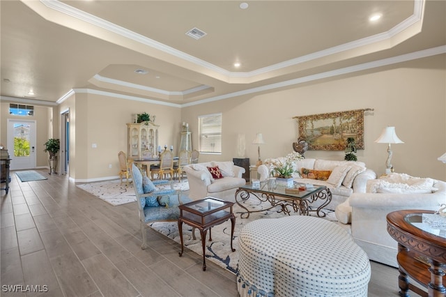 living room with wood-type flooring, ornamental molding, and a raised ceiling