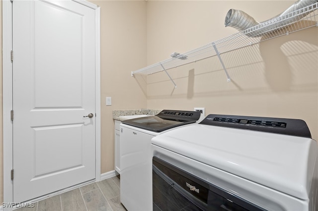 clothes washing area featuring cabinets, light hardwood / wood-style floors, and washer and dryer