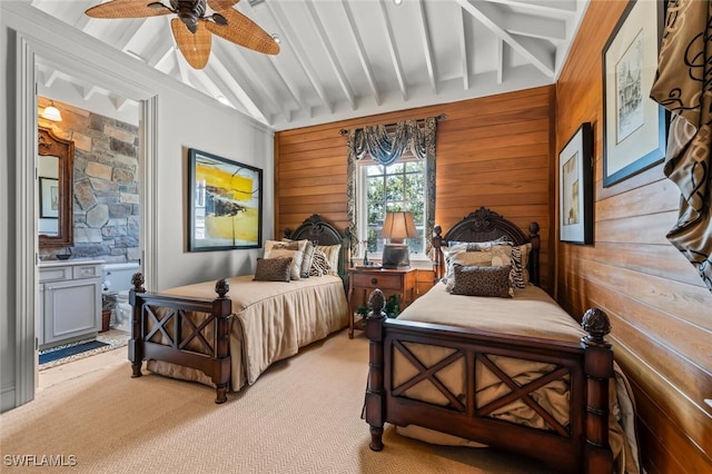 carpeted bedroom featuring ensuite bath, ceiling fan, wood walls, and vaulted ceiling with beams