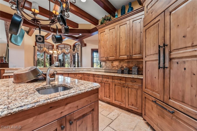 kitchen featuring an inviting chandelier, sink, decorative backsplash, beam ceiling, and light stone counters