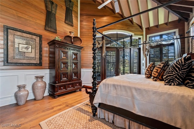 bedroom featuring beamed ceiling, wood walls, hardwood / wood-style floors, and high vaulted ceiling