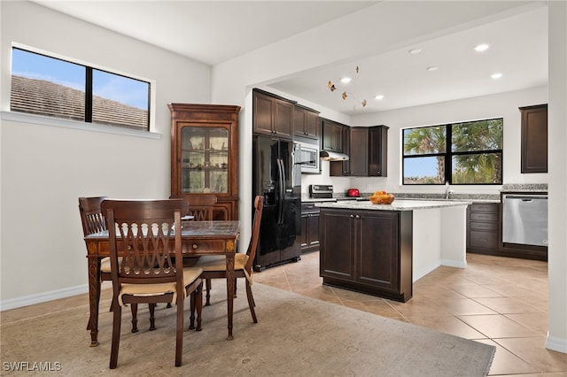 kitchen with dark brown cabinetry, a kitchen island, light tile patterned floors, and appliances with stainless steel finishes