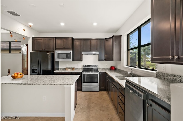 kitchen featuring light stone counters, dark brown cabinets, stainless steel appliances, sink, and a center island