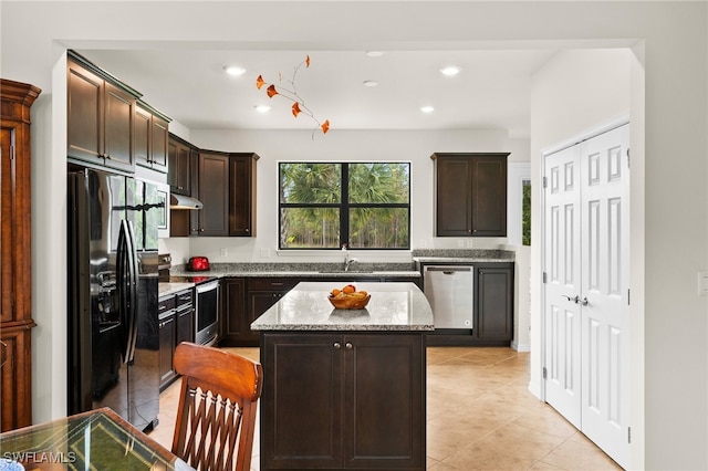 kitchen featuring dark brown cabinetry, light stone countertops, a kitchen island, and appliances with stainless steel finishes