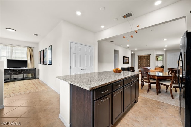 kitchen featuring light stone countertops, a center island, stainless steel fridge, dark brown cabinets, and light tile patterned floors