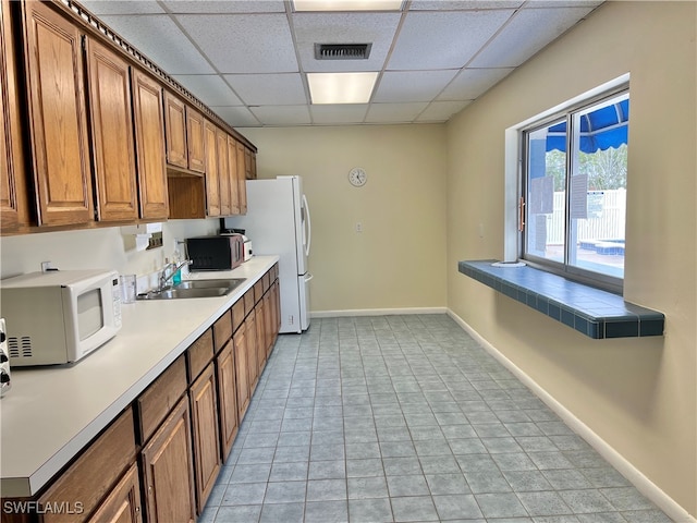 kitchen featuring a drop ceiling, white appliances, sink, and light tile patterned floors