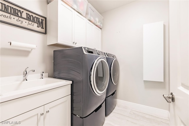 laundry area featuring washer and clothes dryer, cabinets, light wood-type flooring, and sink