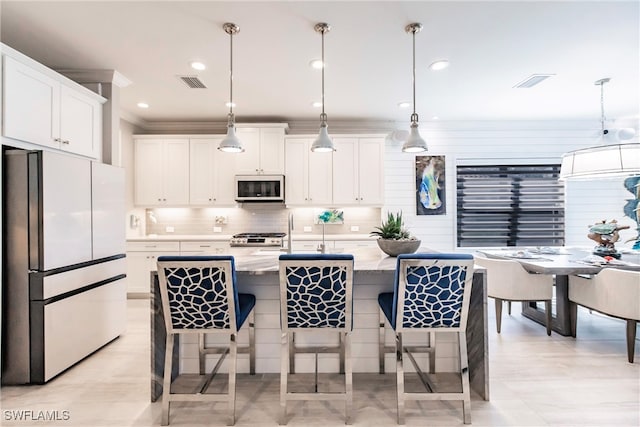 kitchen featuring decorative light fixtures, white cabinetry, a breakfast bar area, and appliances with stainless steel finishes