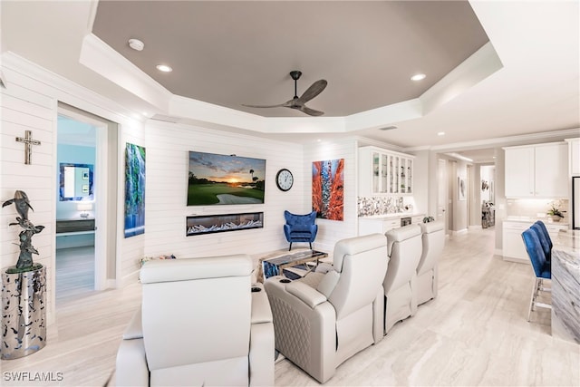 cinema room with light wood-type flooring, a tray ceiling, and ceiling fan