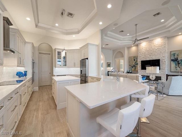 kitchen featuring black electric stovetop, a raised ceiling, a spacious island, sink, and decorative light fixtures