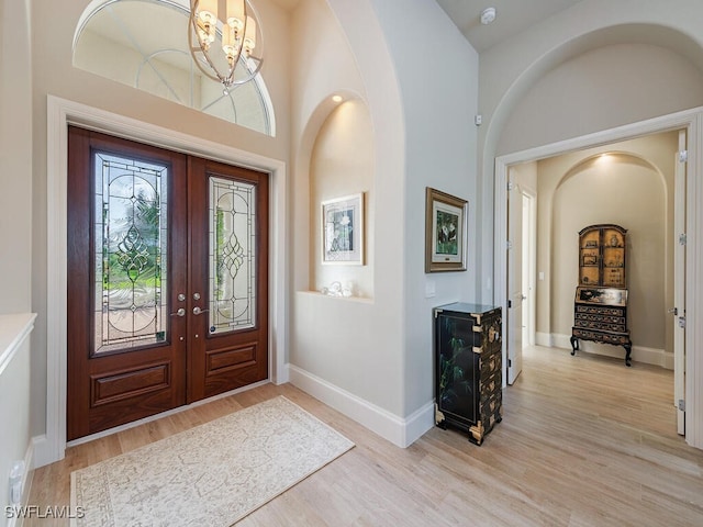 entryway featuring light wood-type flooring, a towering ceiling, and french doors