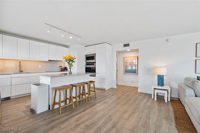 kitchen with a center island, light hardwood / wood-style floors, a kitchen bar, white cabinetry, and stainless steel appliances