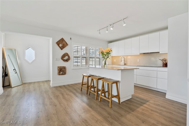 kitchen featuring sink, a kitchen island, a kitchen breakfast bar, light hardwood / wood-style floors, and white cabinets