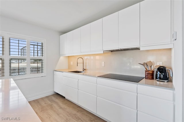 kitchen with backsplash, black electric cooktop, sink, light hardwood / wood-style flooring, and white cabinets