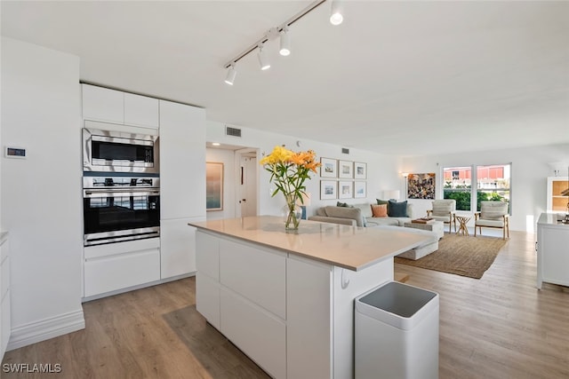 kitchen with stainless steel appliances, white cabinetry, a kitchen island, and light hardwood / wood-style flooring