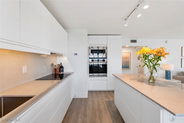 kitchen with white cabinetry, light wood-type flooring, track lighting, and appliances with stainless steel finishes