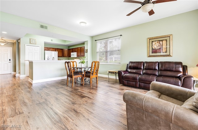 living area featuring light wood finished floors, baseboards, visible vents, and a ceiling fan