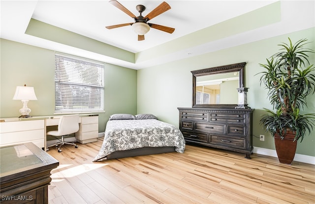 bedroom featuring light wood-type flooring, ceiling fan, baseboards, and a raised ceiling