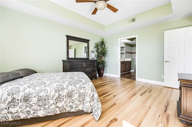 bedroom with a raised ceiling, visible vents, light wood-style flooring, ensuite bath, and baseboards