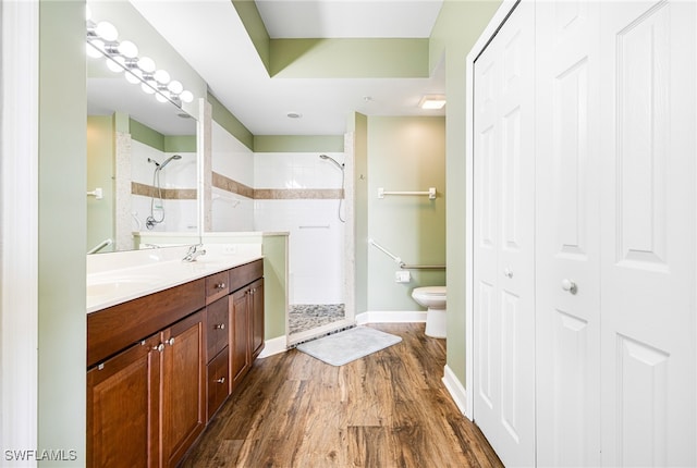 bathroom featuring toilet, wood finished floors, a closet, a shower stall, and double vanity