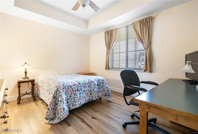 bedroom featuring light wood-type flooring, ceiling fan, baseboards, and a raised ceiling