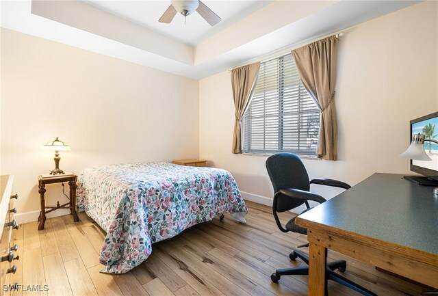 bedroom featuring light wood-style floors, ceiling fan, baseboards, and a tray ceiling