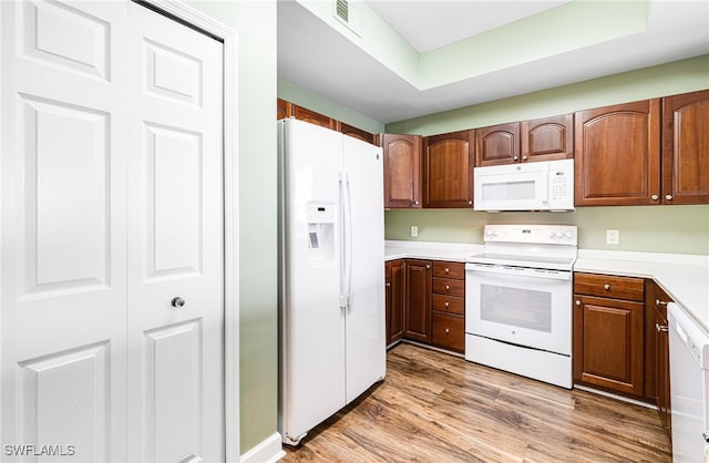 kitchen featuring a tray ceiling, light countertops, visible vents, light wood-style floors, and white appliances