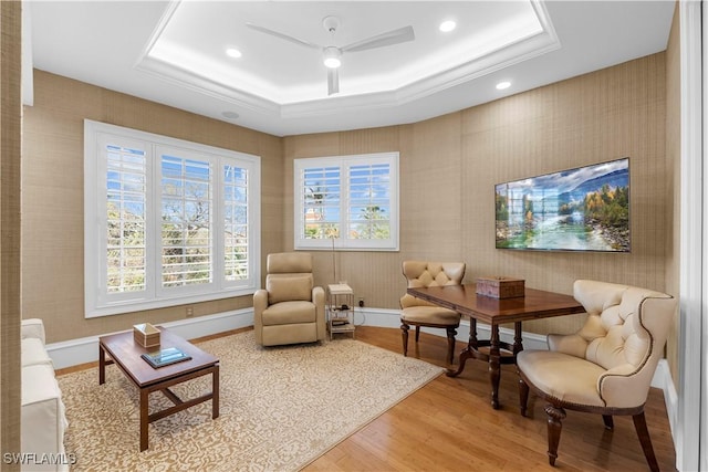 living area featuring hardwood / wood-style floors, a raised ceiling, and ceiling fan