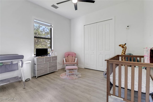 bedroom featuring ceiling fan, a closet, light hardwood / wood-style floors, and a nursery area