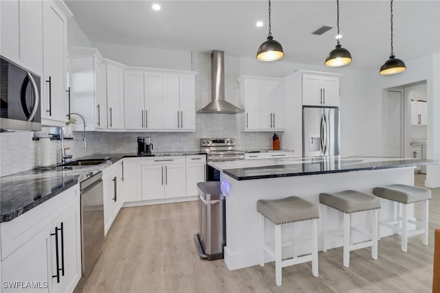 kitchen with stainless steel appliances, a kitchen island, white cabinetry, and wall chimney exhaust hood