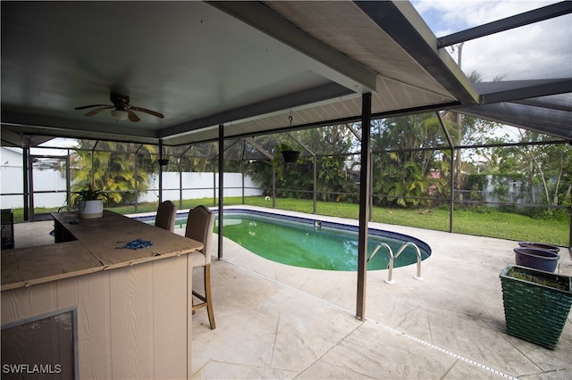 view of pool featuring ceiling fan, glass enclosure, a patio area, an outdoor bar, and a lawn