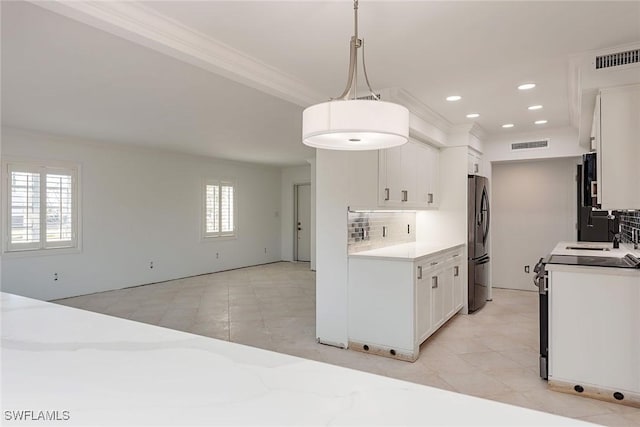 kitchen featuring stove, white cabinets, hanging light fixtures, stainless steel fridge, and tasteful backsplash