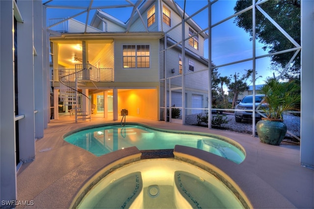 pool at dusk with an in ground hot tub, a patio, and glass enclosure