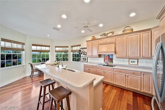 kitchen featuring a kitchen breakfast bar, stainless steel fridge, sink, wood-type flooring, and a center island with sink